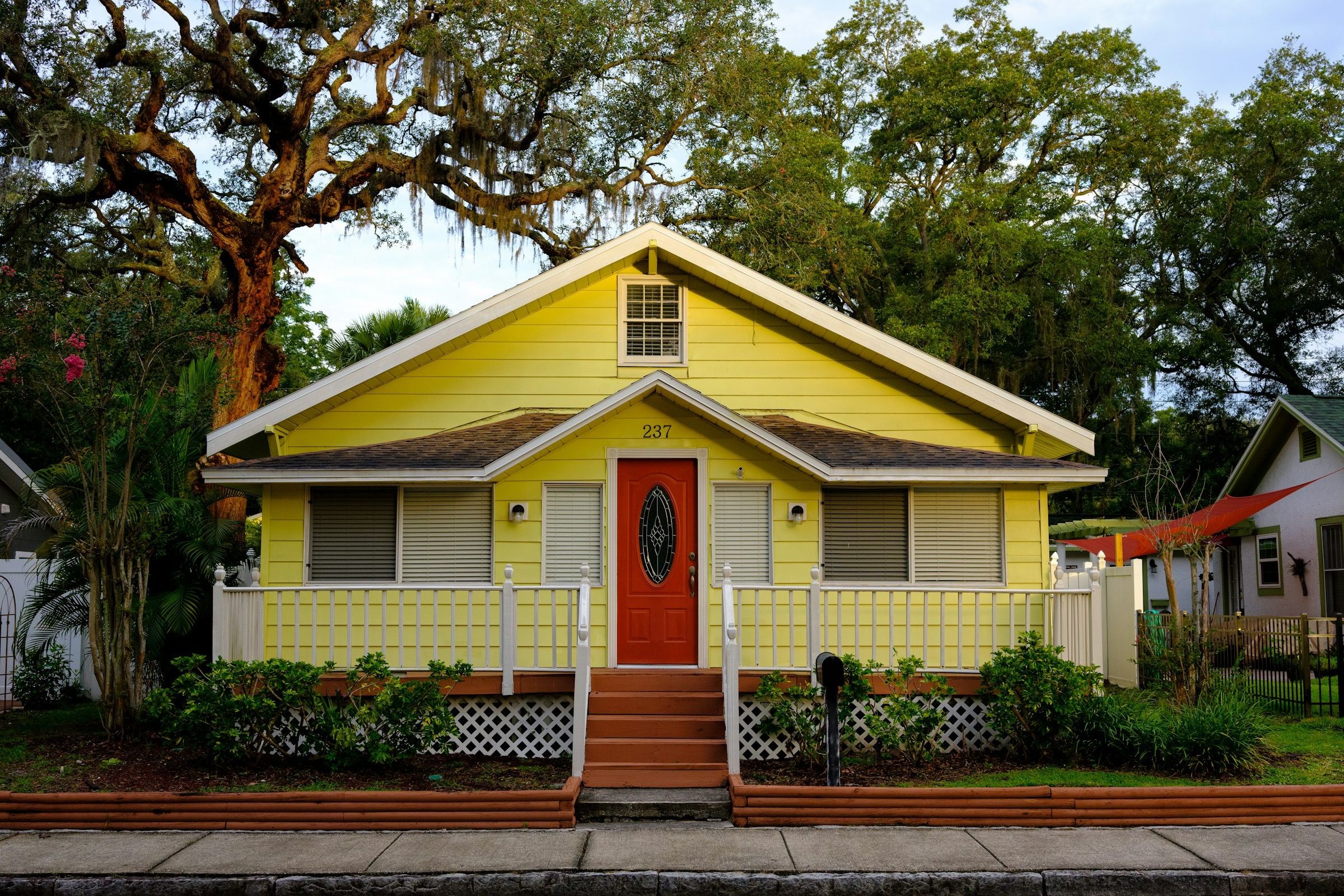 Yellow Florida bungalow with a front porch under live oaks